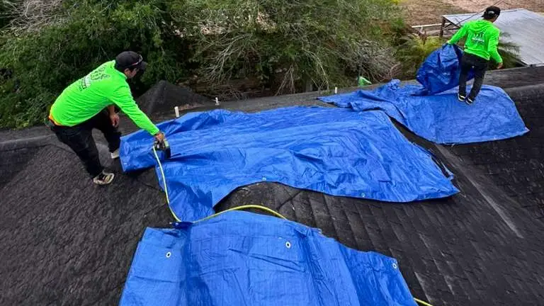 Marva Roofing crew placing blue tarps on a shingle roof for temporary protection