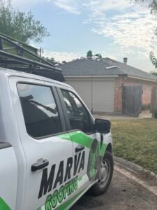 Marva Roofing truck beside a brick home while crew members work on the shingle roof.
