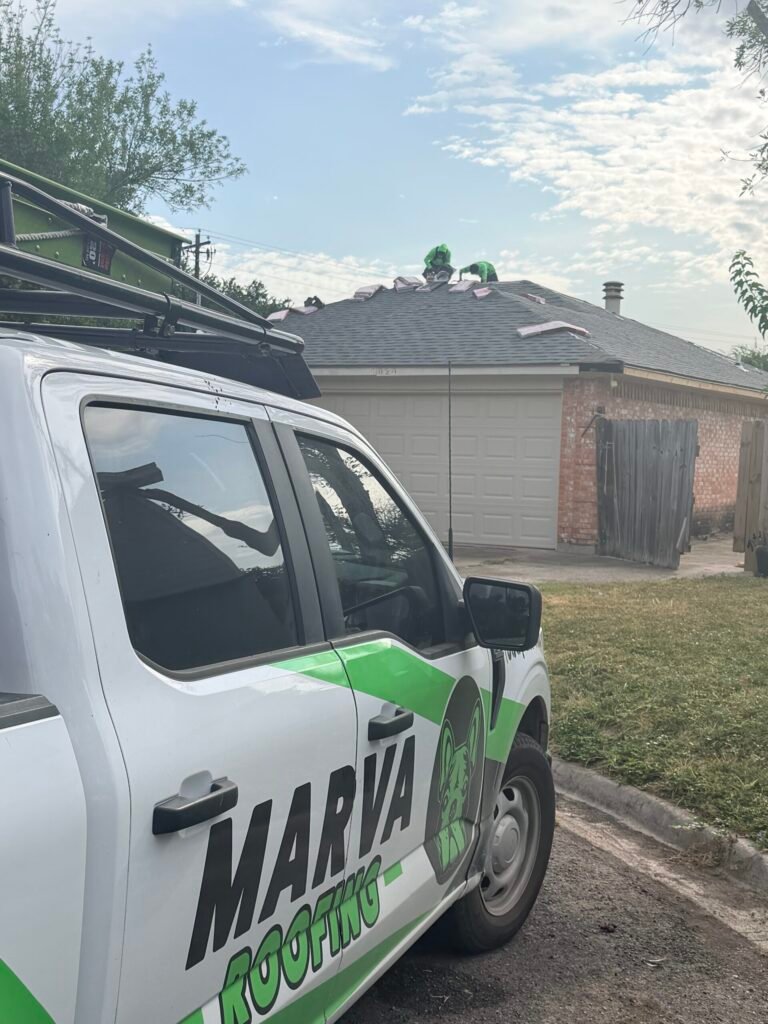 Marva Roofing truck beside a brick home while crew members work on the shingle roof.