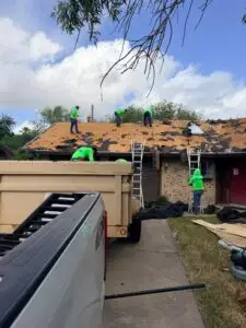 Roofing crew removing old roofing from a house with exposed wood decking.