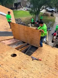 Marva Roofing crew handling a wood roof panel above exposed framing and insulation during roof work.