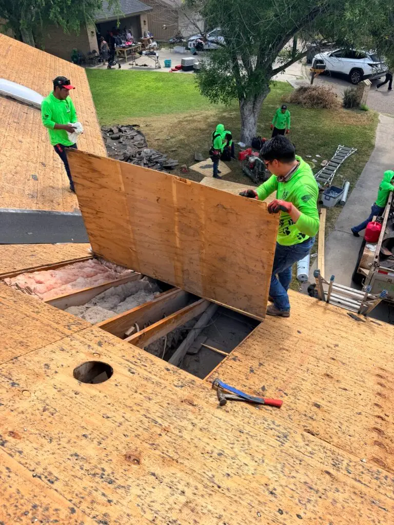 Marva Roofing crew handling a wood roof panel above exposed framing and insulation during roof work.